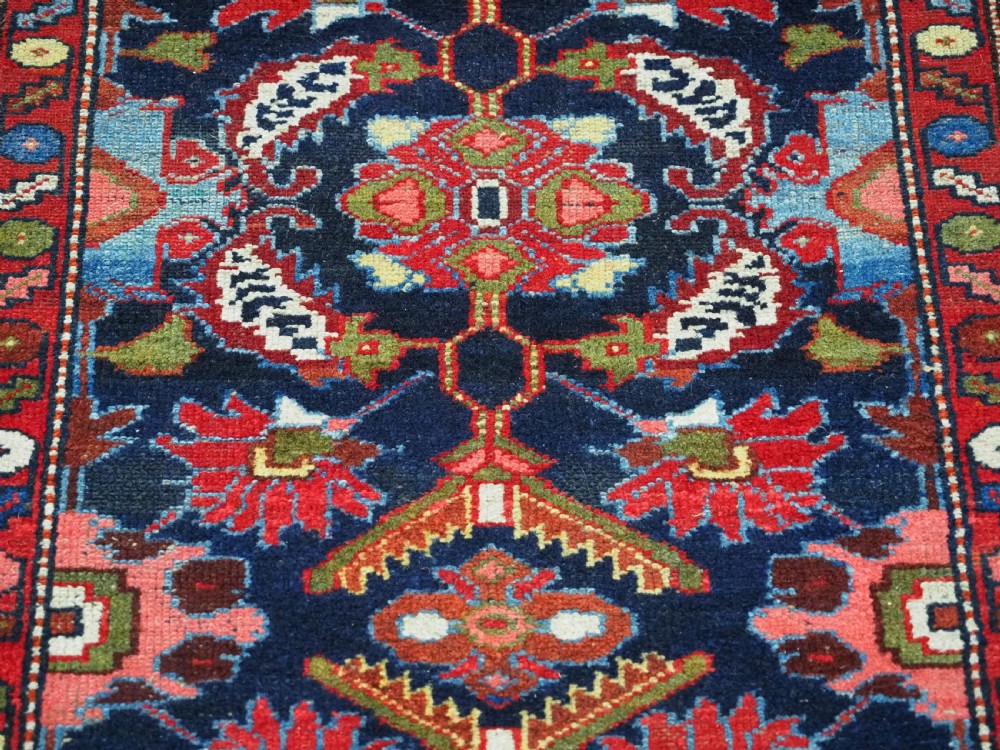 An antique long hand-knotted Persian Hamadan runner rug featuring geometric medallions in shades of dark blue, red, cream, and terracotta. View X