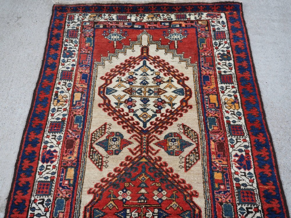 An antique Persian Sarab runner rug featuring repeating geometric diamond medallions on a camel beige central field with terracotta red and navy borders. View III