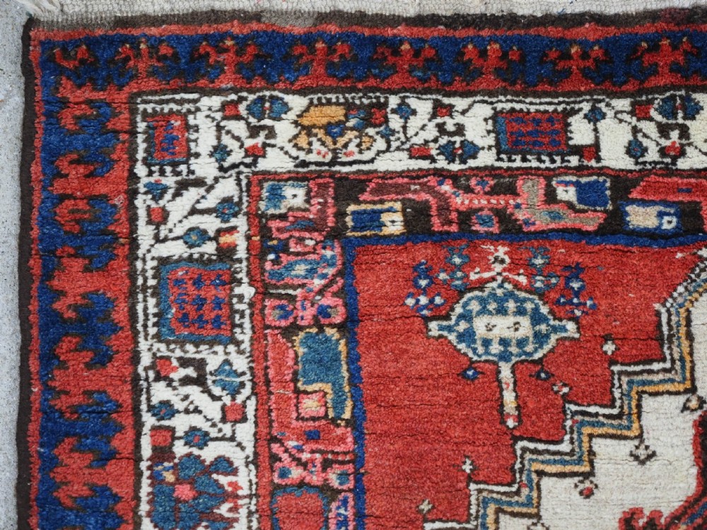 An antique Persian Sarab runner rug featuring repeating geometric diamond medallions on a camel beige central field with terracotta red and navy borders. View VI