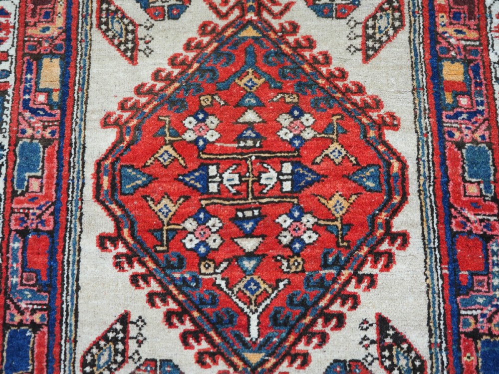 An antique Persian Sarab runner rug featuring repeating geometric diamond medallions on a camel beige central field with terracotta red and navy borders. View VII