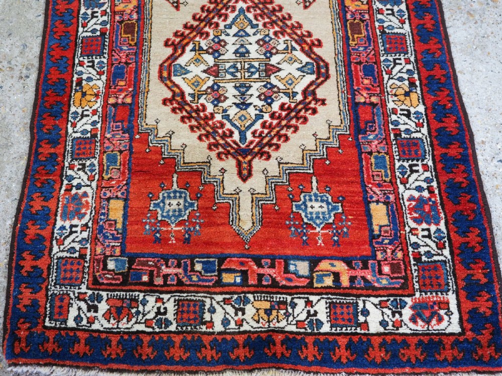 An antique Persian Sarab runner rug featuring repeating geometric diamond medallions on a camel beige central field with terracotta red and navy borders. View VIII