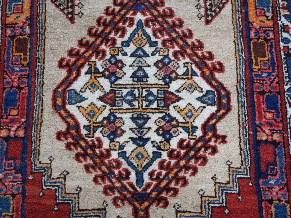 An antique Persian Sarab runner rug featuring repeating geometric diamond medallions on a camel beige central field with terracotta red and navy borders. View IX
