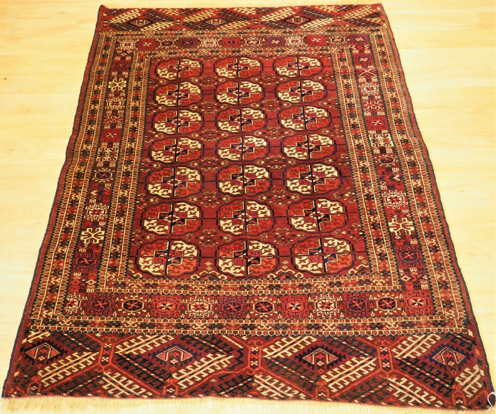 An antique hand-knotted Tekke Turkmen wool rug featuring repeating octagonal gul motifs across a deep red field with detailed geometric borders.