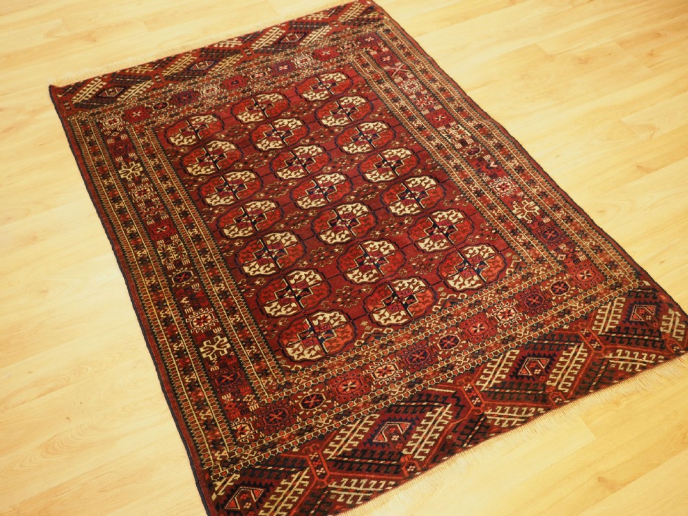 An antique hand-knotted Tekke Turkmen wool rug featuring repeating octagonal gul motifs across a deep red field with detailed geometric borders. View II