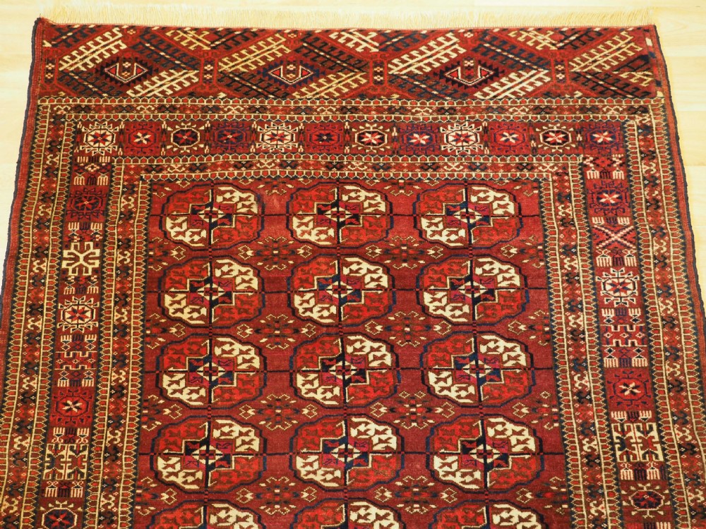 An antique hand-knotted Tekke Turkmen wool rug featuring repeating octagonal gul motifs across a deep red field with detailed geometric borders. View III