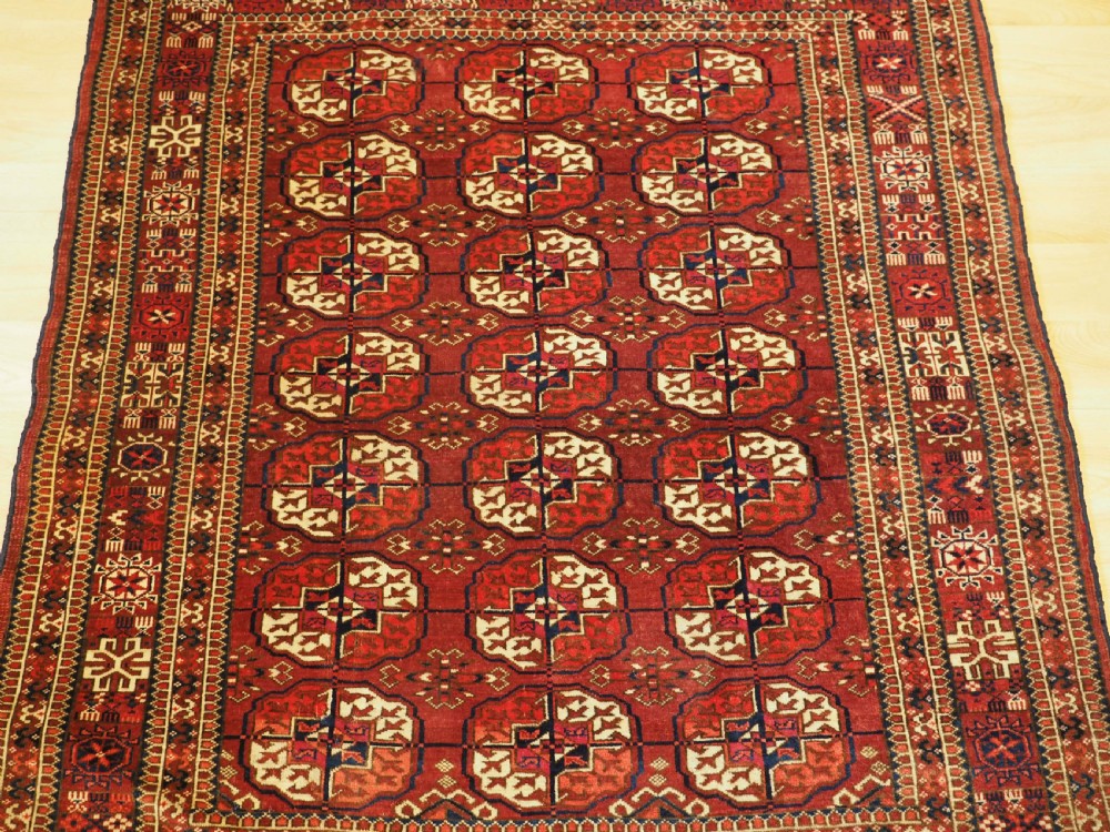 An antique hand-knotted Tekke Turkmen wool rug featuring repeating octagonal gul motifs across a deep red field with detailed geometric borders. View IV
