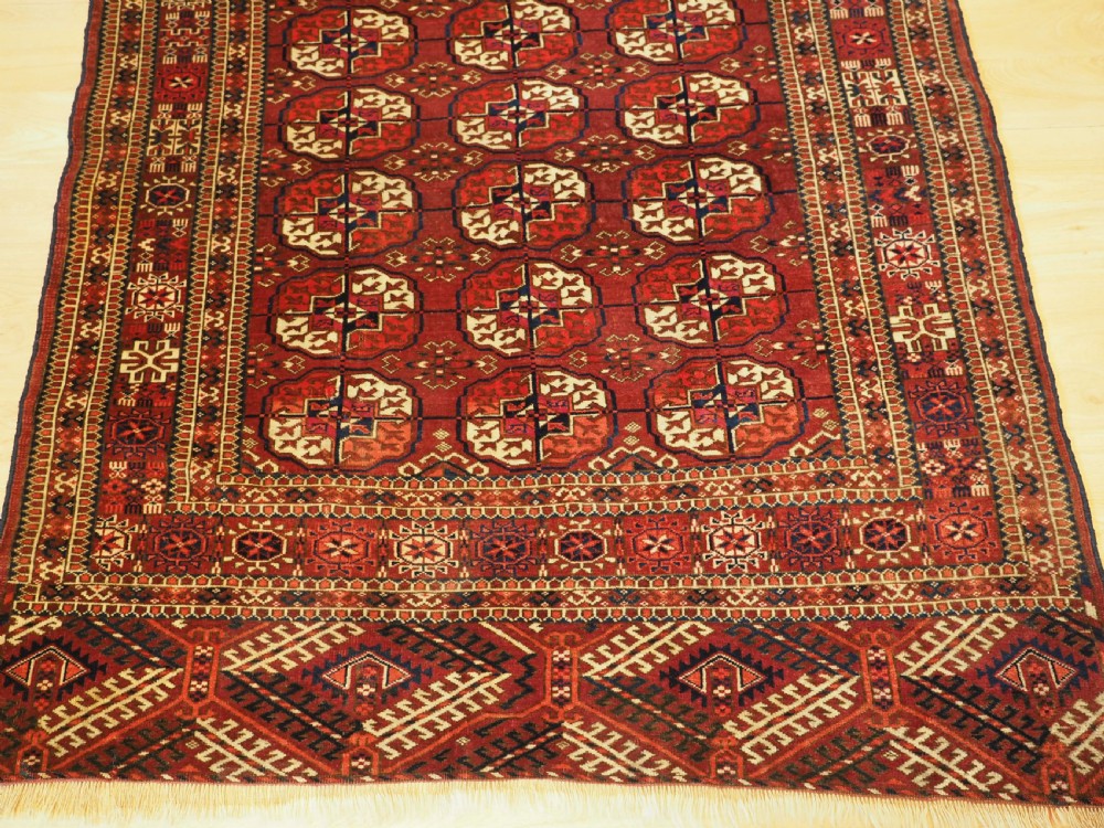An antique hand-knotted Tekke Turkmen wool rug featuring repeating octagonal gul motifs across a deep red field with detailed geometric borders. View V
