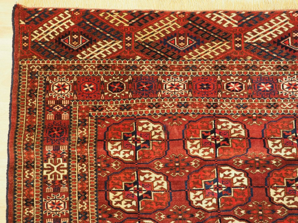 An antique hand-knotted Tekke Turkmen wool rug featuring repeating octagonal gul motifs across a deep red field with detailed geometric borders. View VI