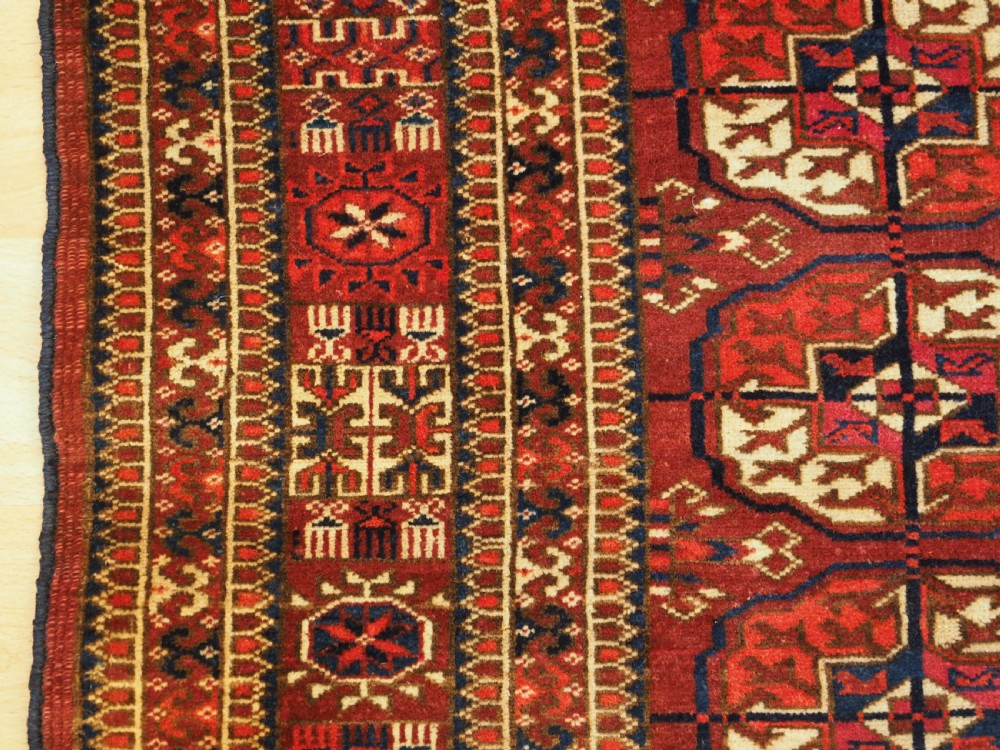 An antique hand-knotted Tekke Turkmen wool rug featuring repeating octagonal gul motifs across a deep red field with detailed geometric borders. View VII