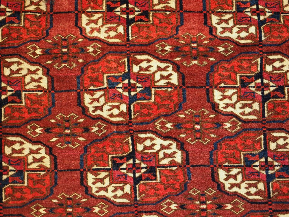 An antique hand-knotted Tekke Turkmen wool rug featuring repeating octagonal gul motifs across a deep red field with detailed geometric borders. View VIII