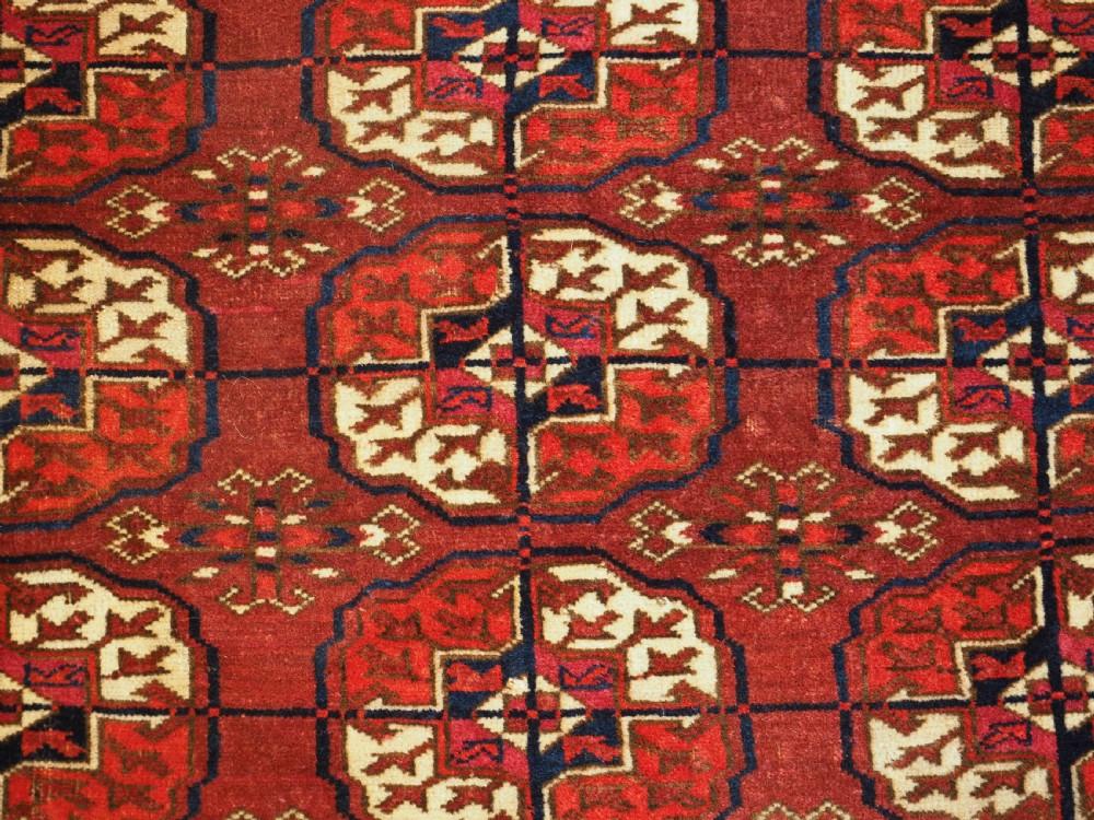 An antique hand-knotted Tekke Turkmen wool rug featuring repeating octagonal gul motifs across a deep red field with detailed geometric borders. View IX