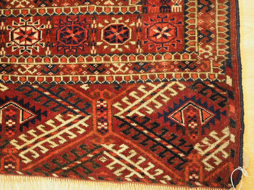An antique hand-knotted Tekke Turkmen wool rug featuring repeating octagonal gul motifs across a deep red field with detailed geometric borders. View X