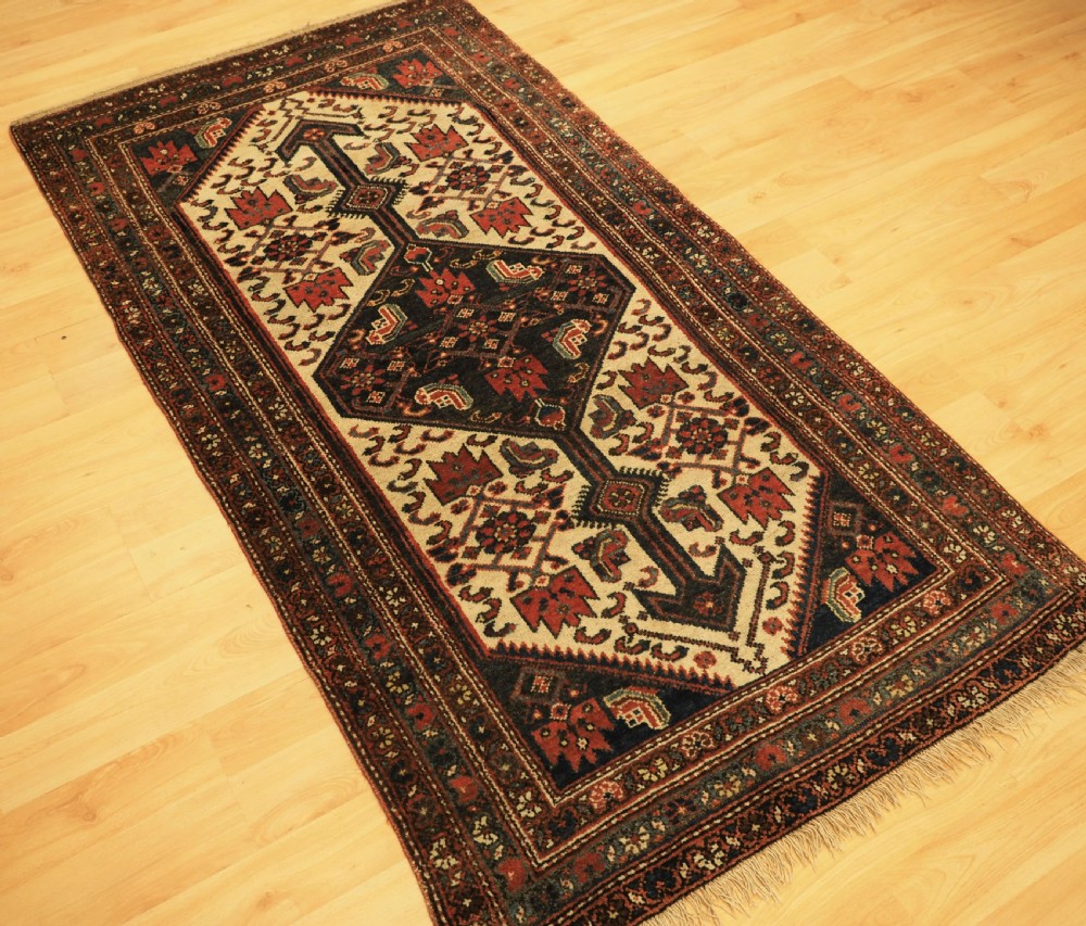 An antique hand-knotted wool rug featuring a central dark blue geometric diamond medallion framed by cream and terracotta field patterns. View II