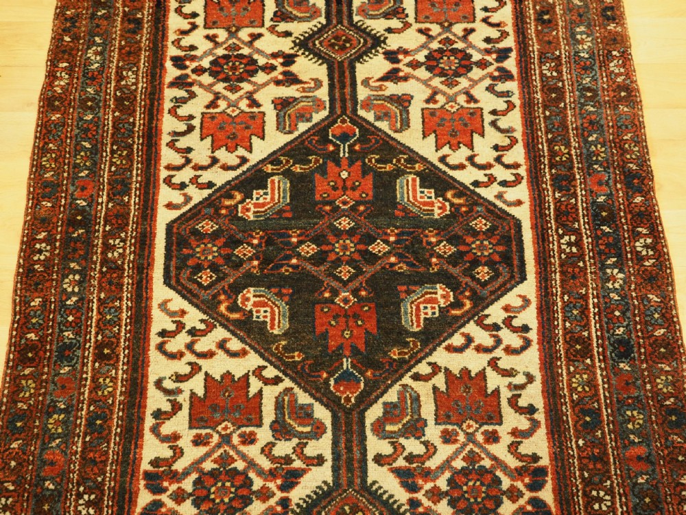 An antique hand-knotted wool rug featuring a central dark blue geometric diamond medallion framed by cream and terracotta field patterns. View III