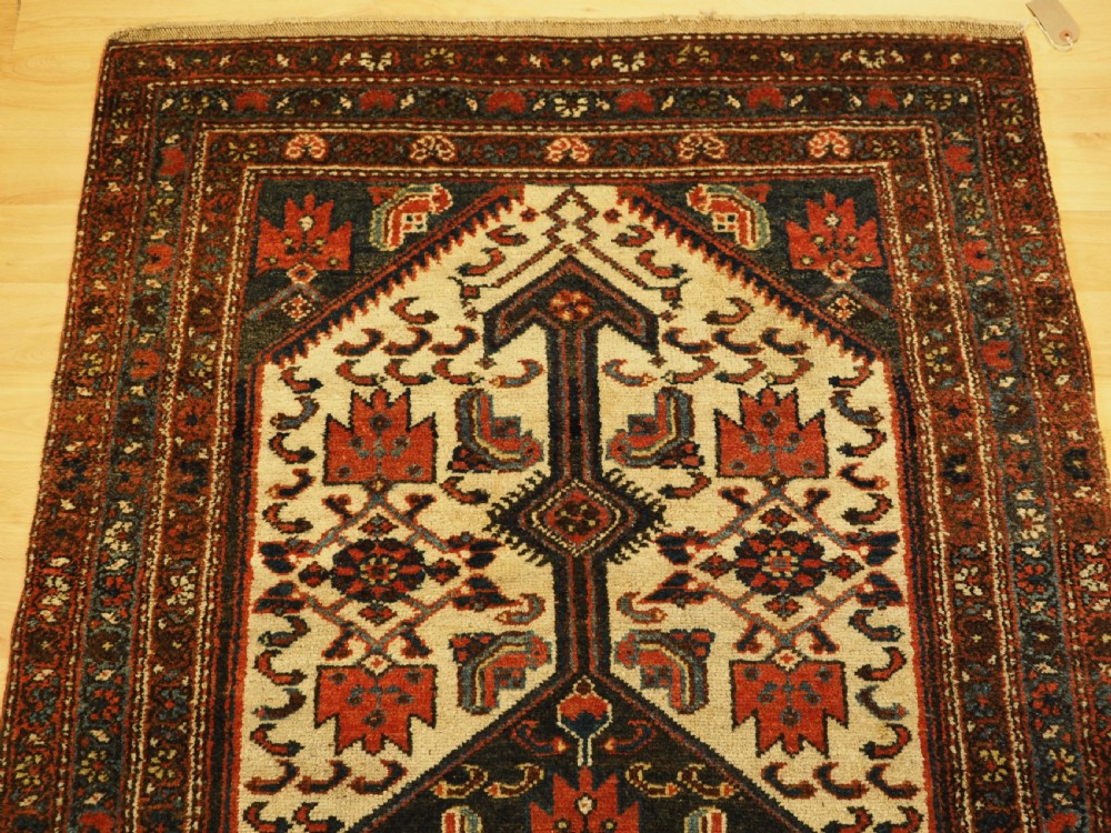 An antique hand-knotted wool rug featuring a central dark blue geometric diamond medallion framed by cream and terracotta field patterns. View IV