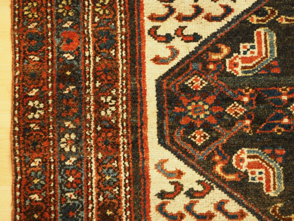 An antique hand-knotted wool rug featuring a central dark blue geometric diamond medallion framed by cream and terracotta field patterns. View V