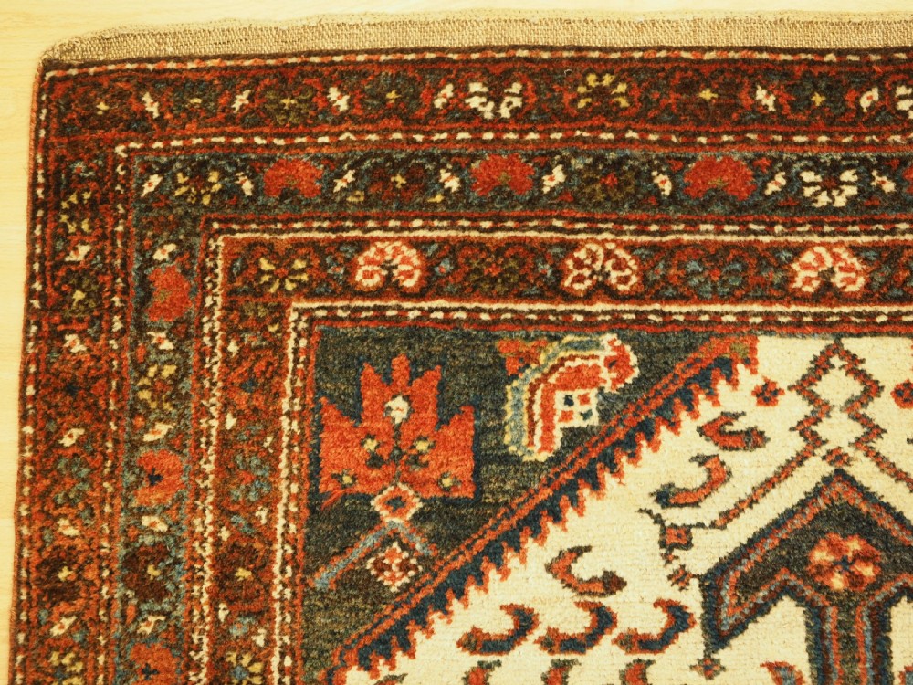 An antique hand-knotted wool rug featuring a central dark blue geometric diamond medallion framed by cream and terracotta field patterns. View VI