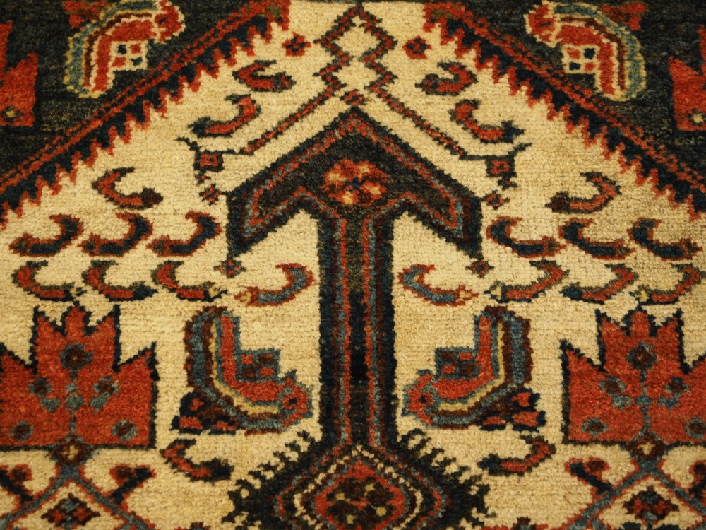 An antique hand-knotted wool rug featuring a central dark blue geometric diamond medallion framed by cream and terracotta field patterns. View VII