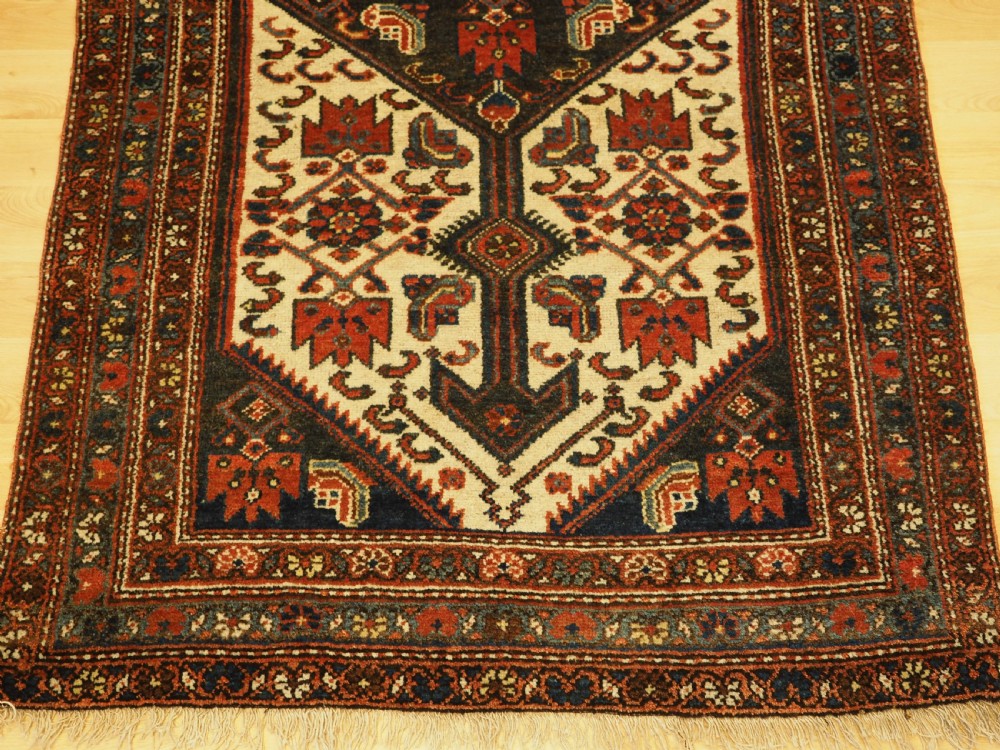 An antique hand-knotted wool rug featuring a central dark blue geometric diamond medallion framed by cream and terracotta field patterns. View X