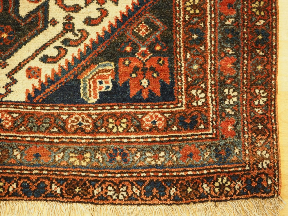 An antique hand-knotted wool rug featuring a central dark blue geometric diamond medallion framed by cream and terracotta field patterns. View XI