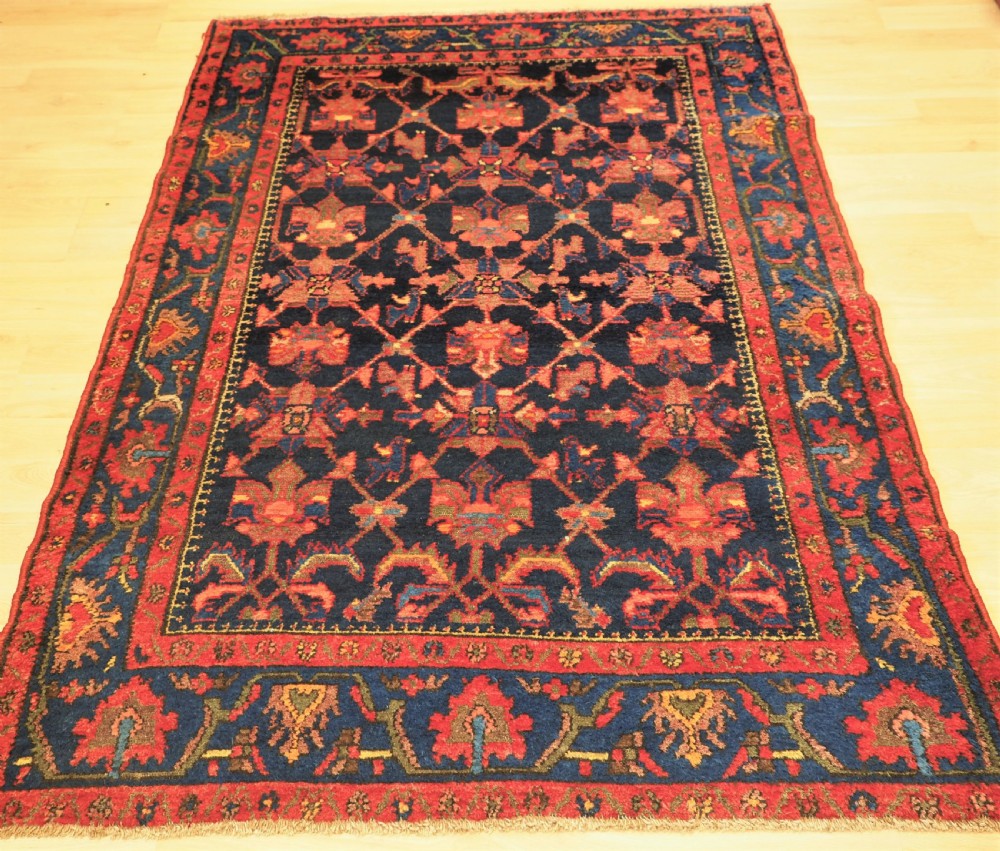 An antique hand-knotted Persian rug featuring a deep navy blue field with a red floral lattice pattern surrounded by a broad patterned border.