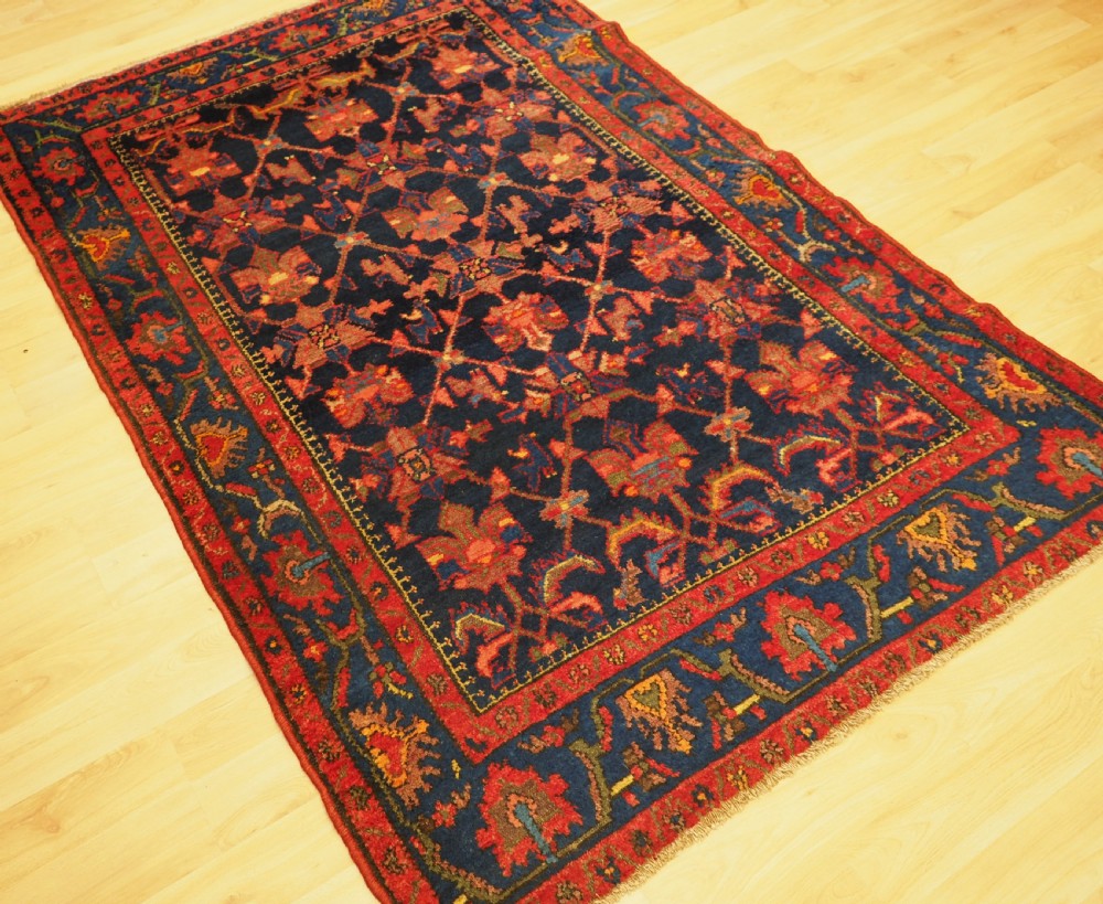 An antique hand-knotted Persian rug featuring a deep navy blue field with a red floral lattice pattern surrounded by a broad patterned border. View II