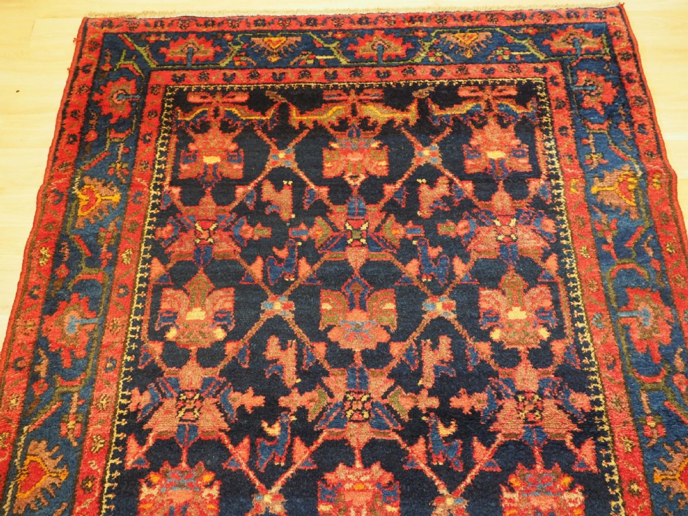 An antique hand-knotted Persian rug featuring a deep navy blue field with a red floral lattice pattern surrounded by a broad patterned border. View III