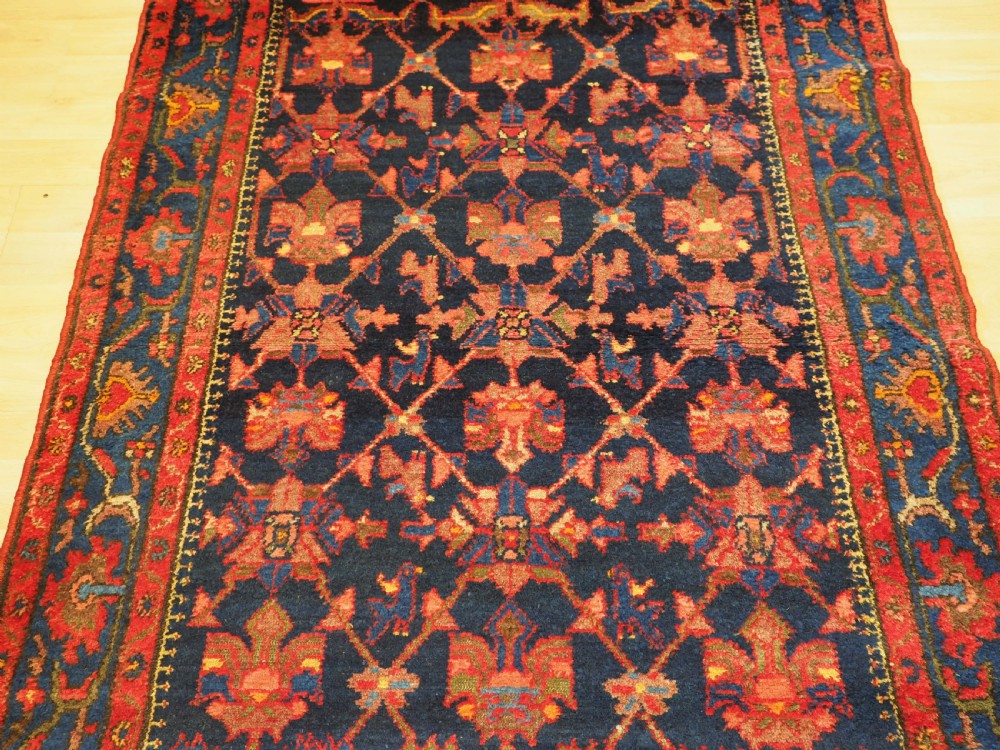 An antique hand-knotted Persian rug featuring a deep navy blue field with a red floral lattice pattern surrounded by a broad patterned border. View IV