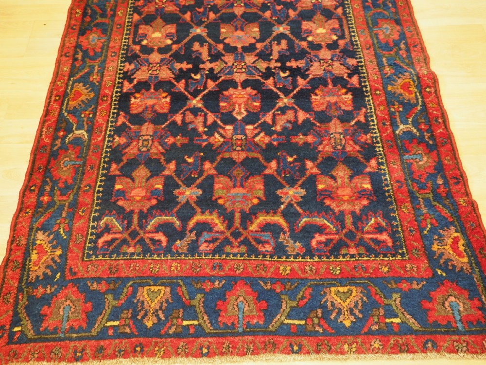 An antique hand-knotted Persian rug featuring a deep navy blue field with a red floral lattice pattern surrounded by a broad patterned border. View V