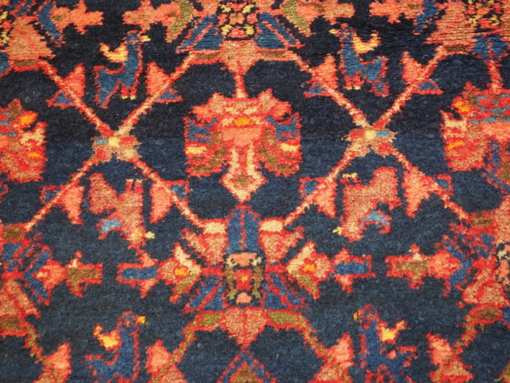 An antique hand-knotted Persian rug featuring a deep navy blue field with a red floral lattice pattern surrounded by a broad patterned border. View VI
