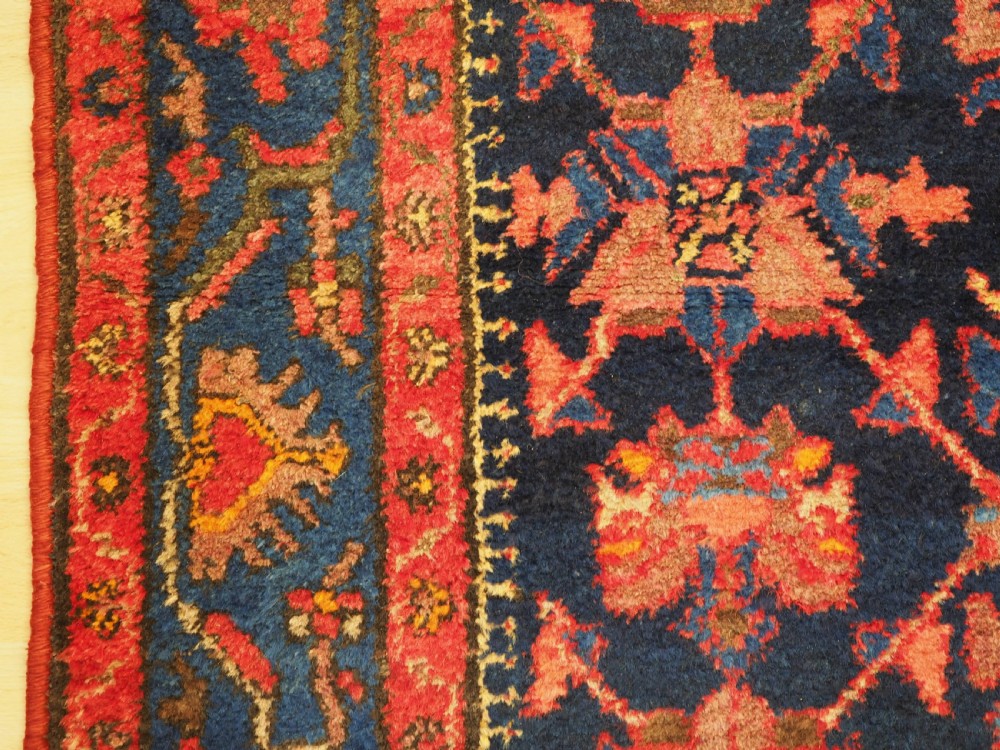 An antique hand-knotted Persian rug featuring a deep navy blue field with a red floral lattice pattern surrounded by a broad patterned border. View VII