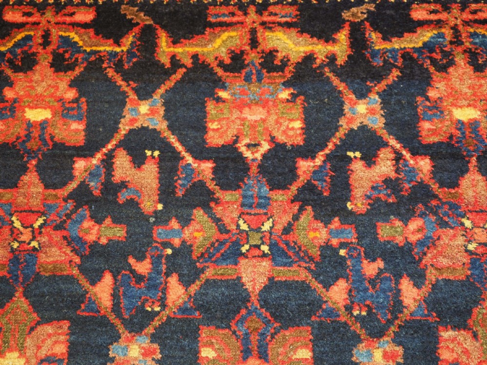 An antique hand-knotted Persian rug featuring a deep navy blue field with a red floral lattice pattern surrounded by a broad patterned border. View IX