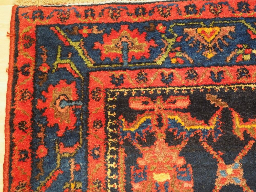 An antique hand-knotted Persian rug featuring a deep navy blue field with a red floral lattice pattern surrounded by a broad patterned border. View X