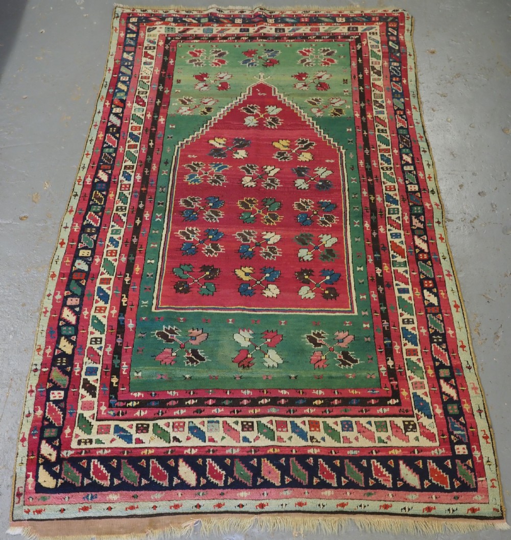 An antique hand-knotted Anatolian Kirsehir prayer rug featuring a central red arch motif framed by green sections and geometric borders.