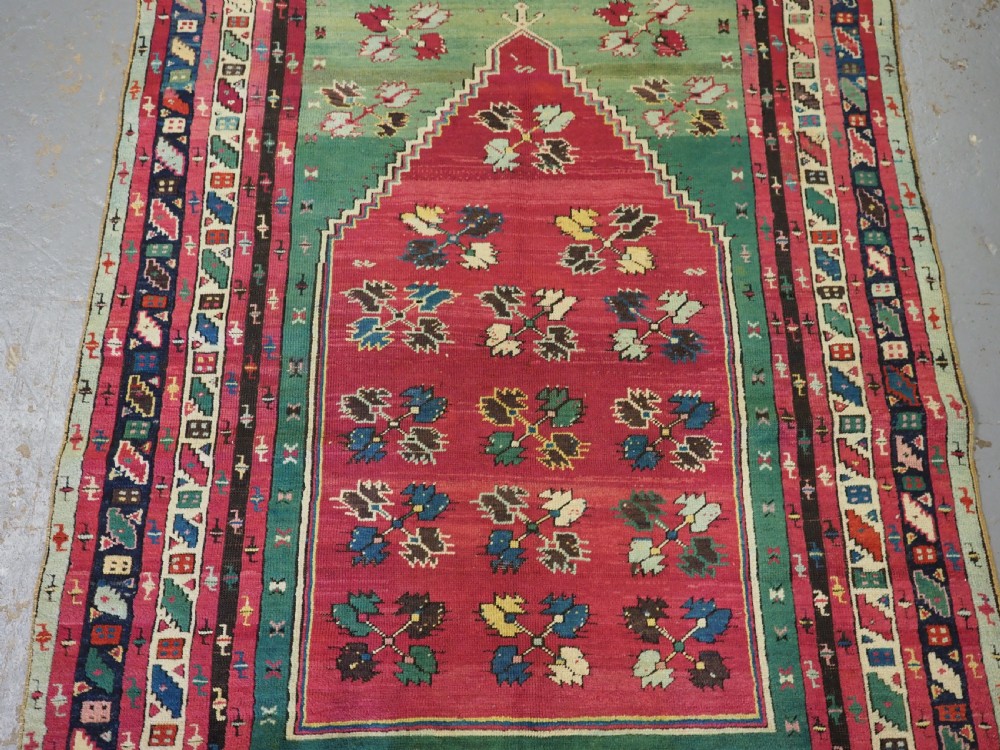 An antique hand-knotted Anatolian Kirsehir prayer rug featuring a central red arch motif framed by green sections and geometric borders. View III