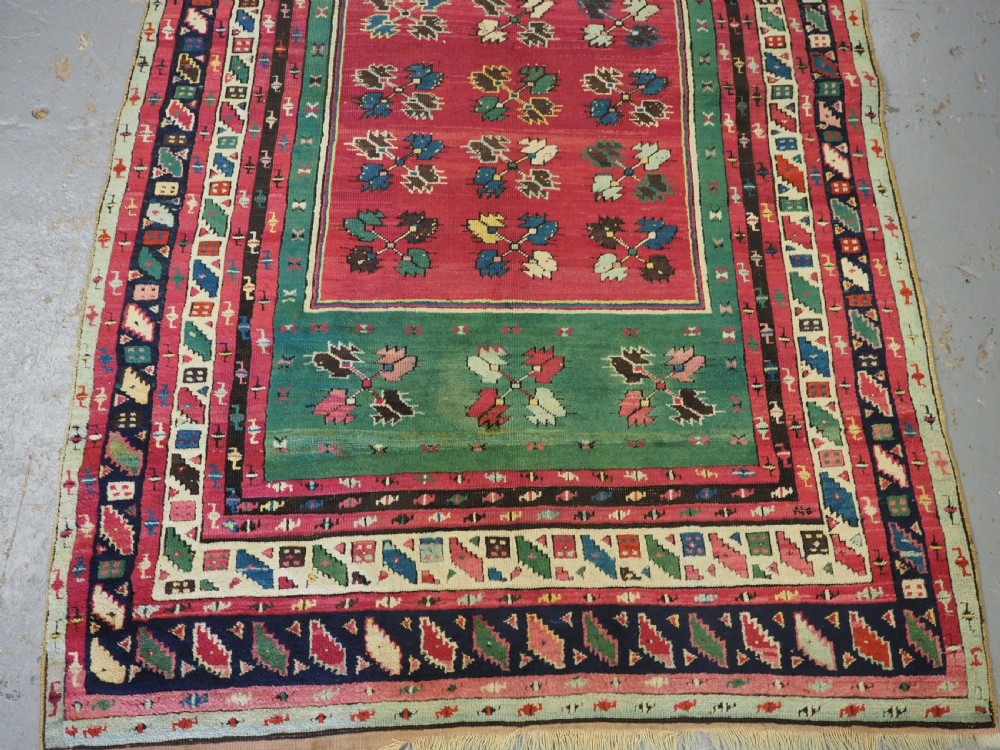 An antique hand-knotted Anatolian Kirsehir prayer rug featuring a central red arch motif framed by green sections and geometric borders. View IV