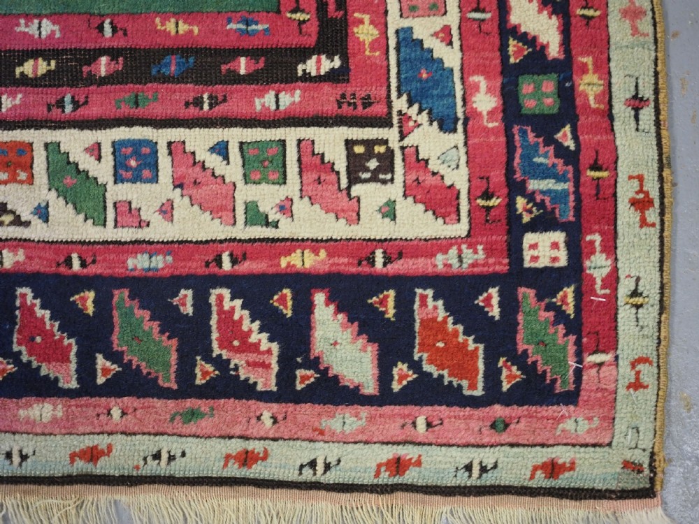 An antique hand-knotted Anatolian Kirsehir prayer rug featuring a central red arch motif framed by green sections and geometric borders. View X