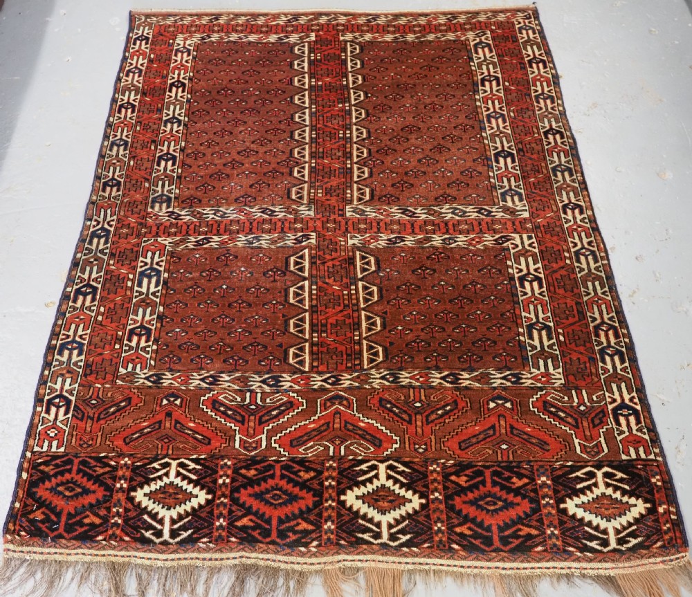 An antique Yomut Turkmen Ensi wool rug featuring a four-part central field design, geometric borders, and an elem end panel in deep red, brown, and ivory.