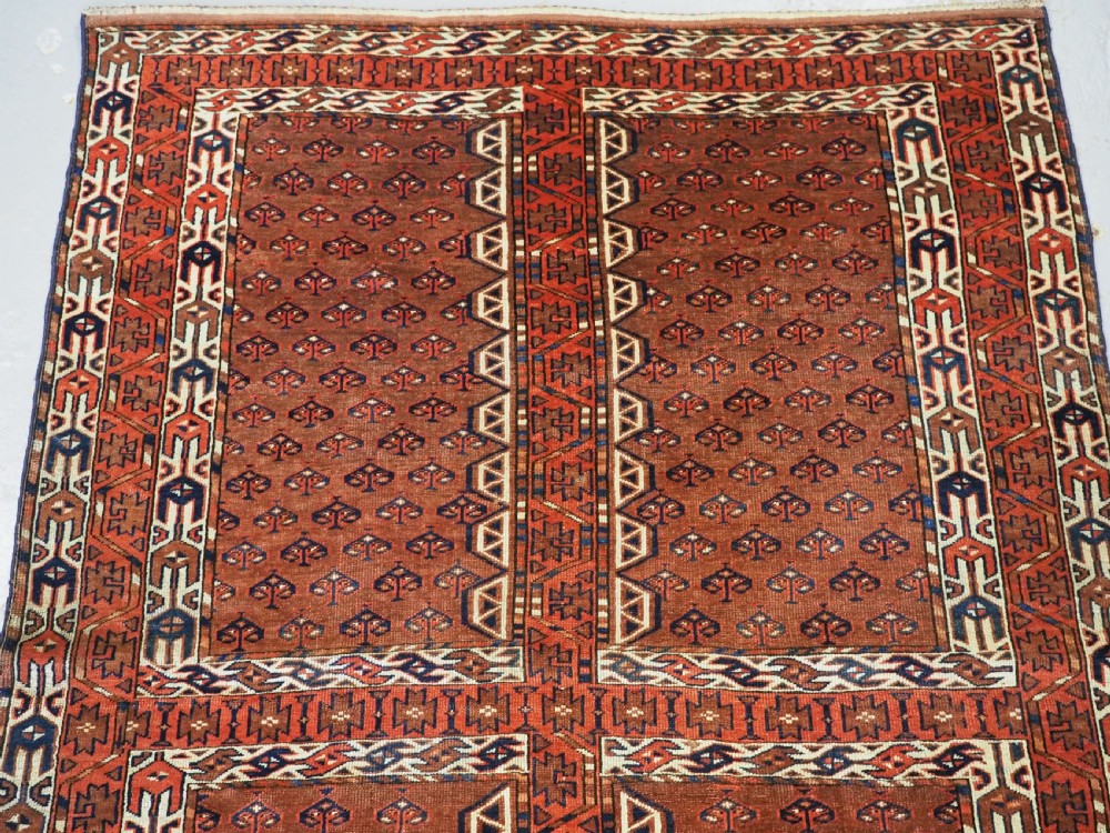 An antique Yomut Turkmen Ensi wool rug featuring a four-part central field design, geometric borders, and an elem end panel in deep red, brown, and ivory. View III