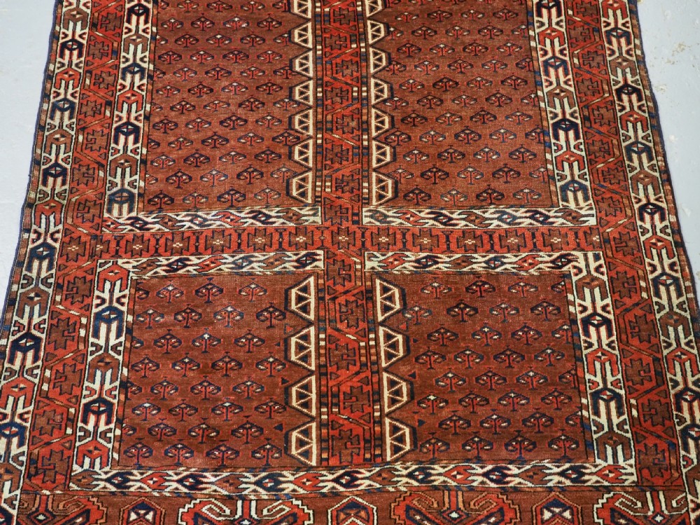 An antique Yomut Turkmen Ensi wool rug featuring a four-part central field design, geometric borders, and an elem end panel in deep red, brown, and ivory. View IV