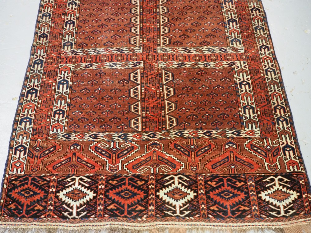An antique Yomut Turkmen Ensi wool rug featuring a four-part central field design, geometric borders, and an elem end panel in deep red, brown, and ivory. View V
