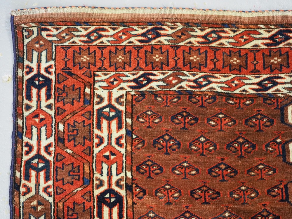 An antique Yomut Turkmen Ensi wool rug featuring a four-part central field design, geometric borders, and an elem end panel in deep red, brown, and ivory. View VI