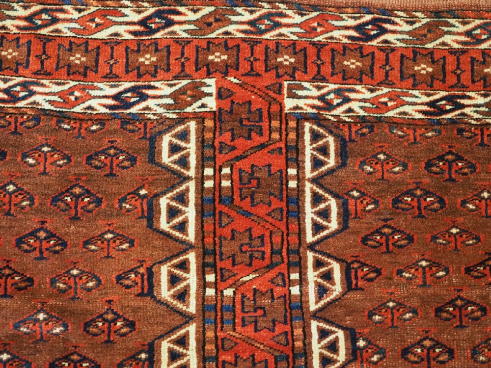 An antique Yomut Turkmen Ensi wool rug featuring a four-part central field design, geometric borders, and an elem end panel in deep red, brown, and ivory. View VII