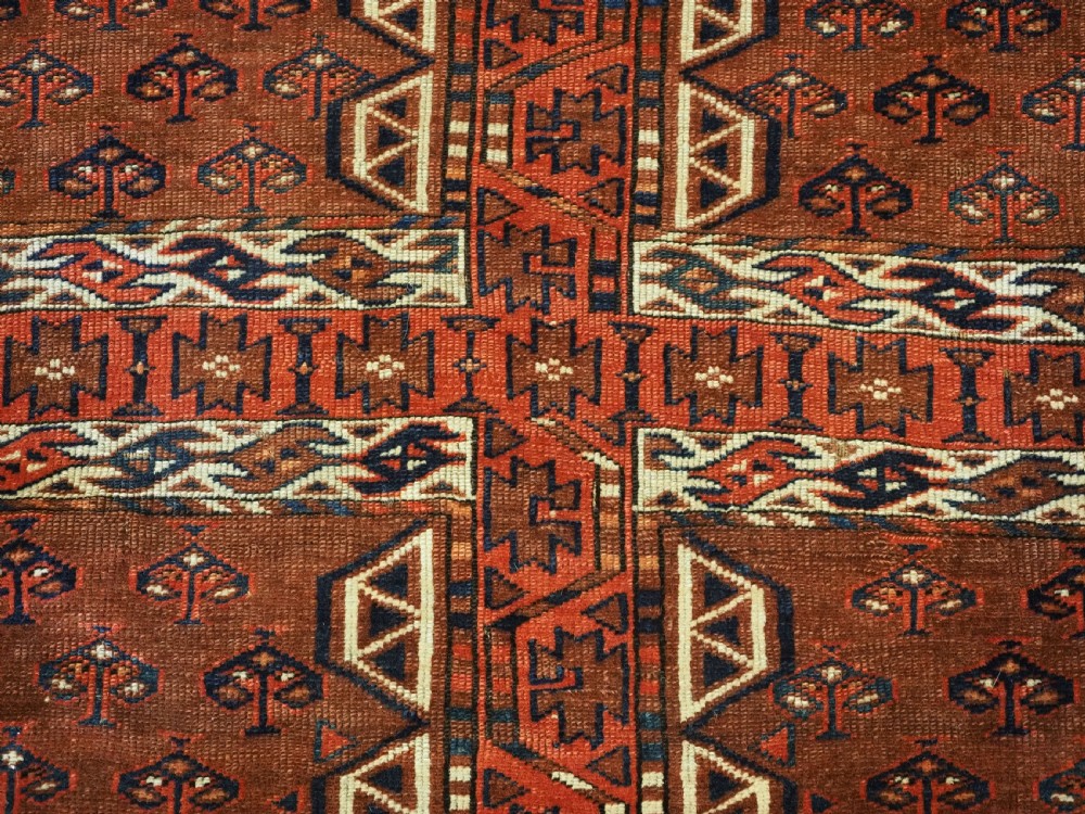 An antique Yomut Turkmen Ensi wool rug featuring a four-part central field design, geometric borders, and an elem end panel in deep red, brown, and ivory. View VIII