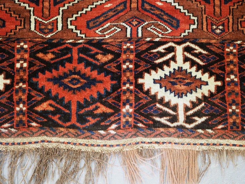 An antique Yomut Turkmen Ensi wool rug featuring a four-part central field design, geometric borders, and an elem end panel in deep red, brown, and ivory. View XI