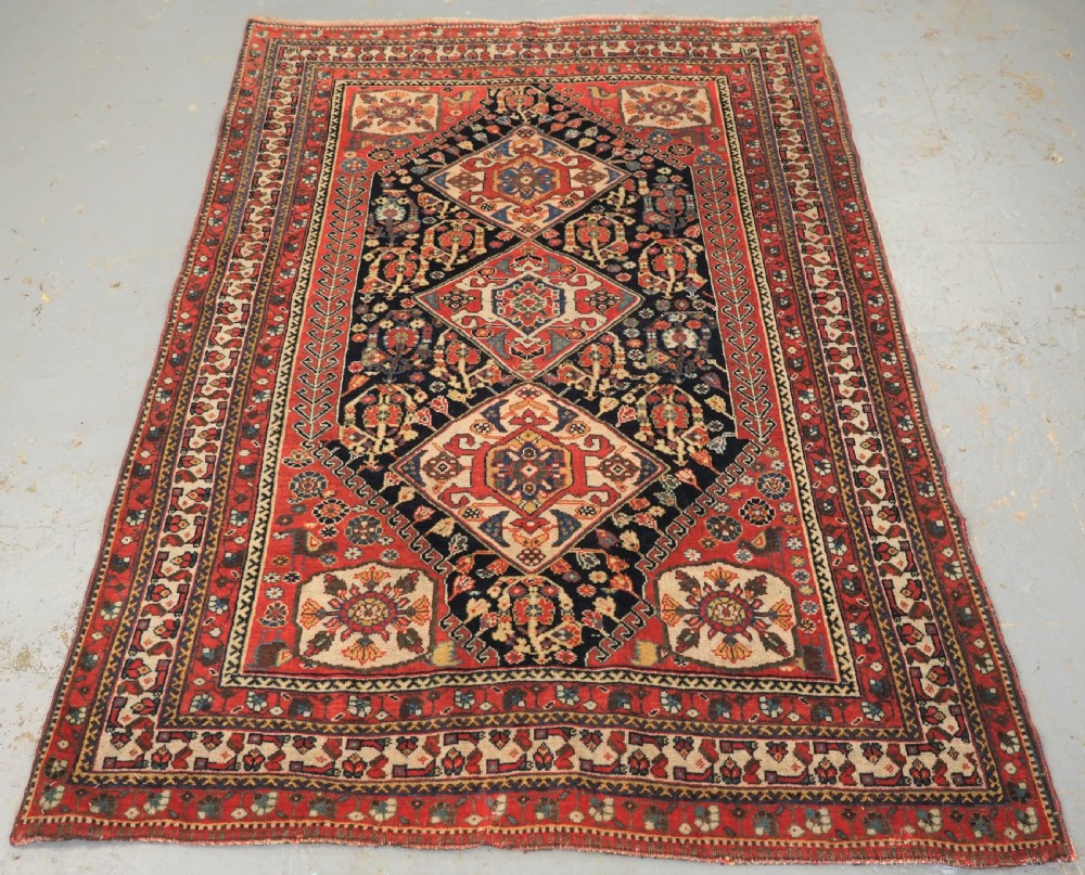 A hand-knotted wool rug featuring three diamond medallions on a dark navy field surrounded by geometric floral borders in red, ivory, and blue.