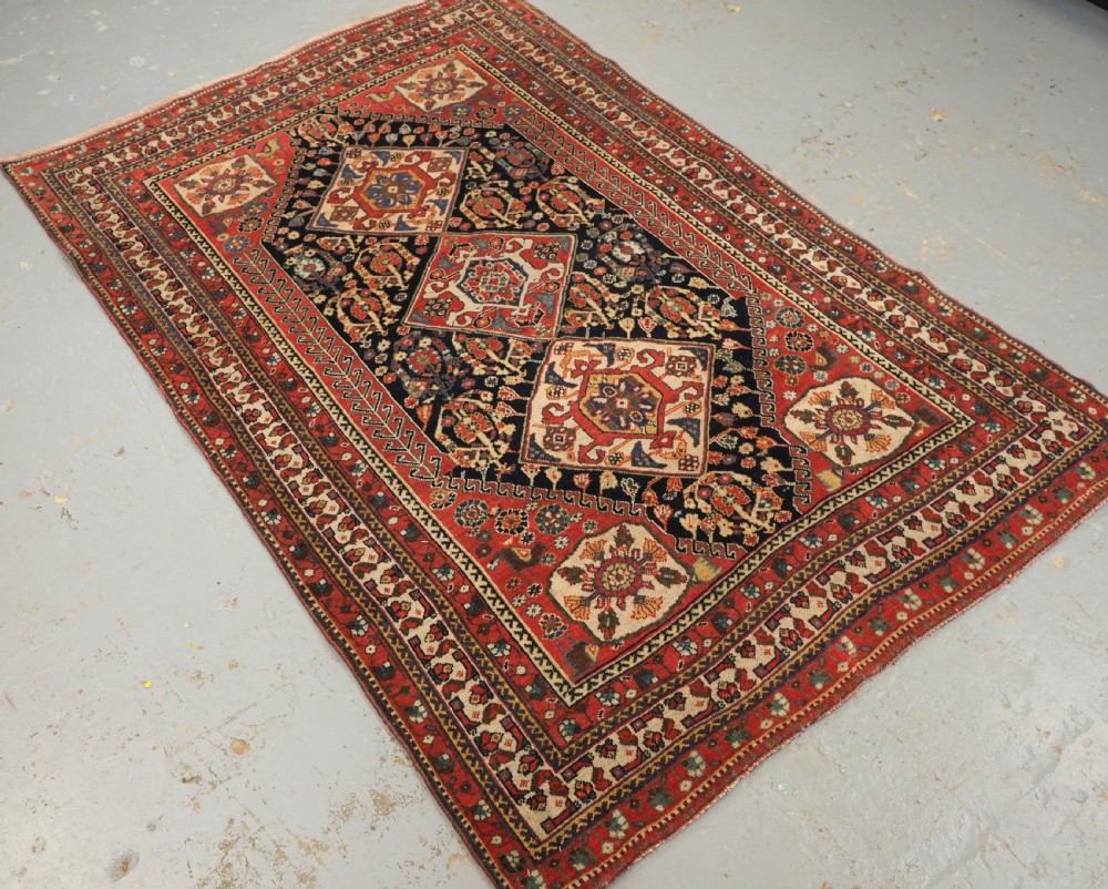 A hand-knotted wool rug featuring three diamond medallions on a dark navy field surrounded by geometric floral borders in red, ivory, and blue. View II