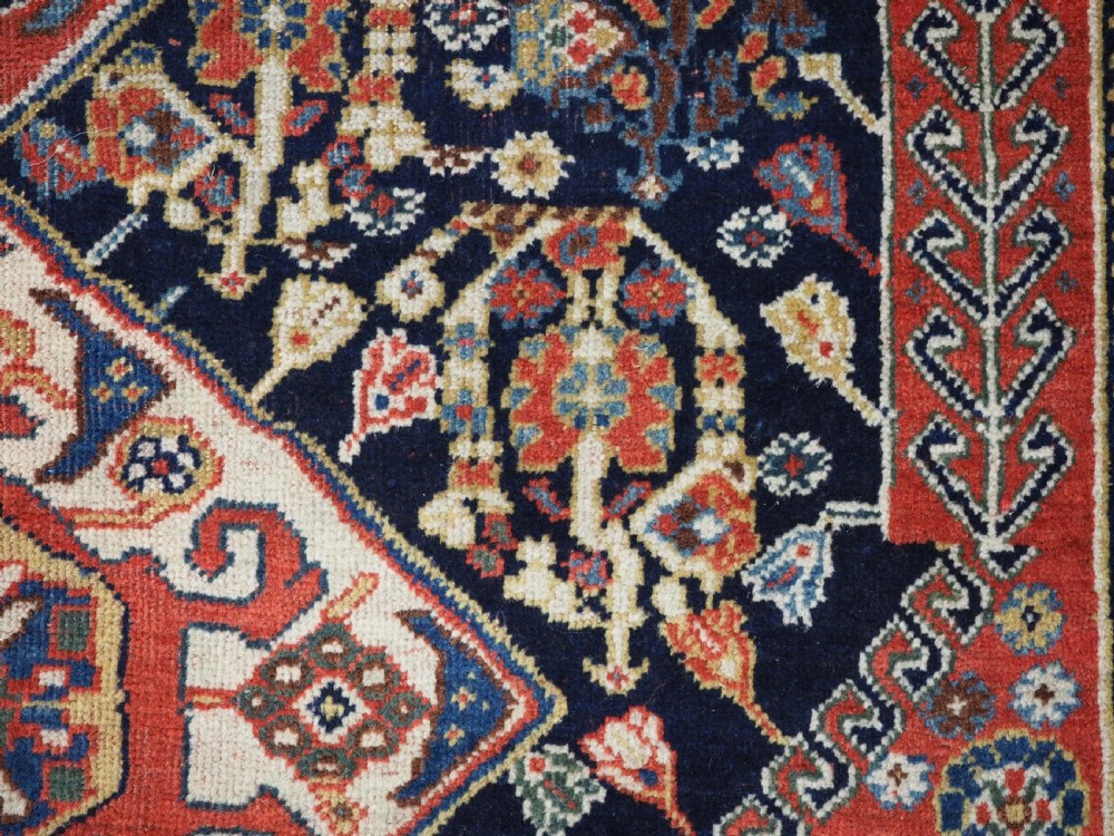 A hand-knotted wool rug featuring three diamond medallions on a dark navy field surrounded by geometric floral borders in red, ivory, and blue. View VII