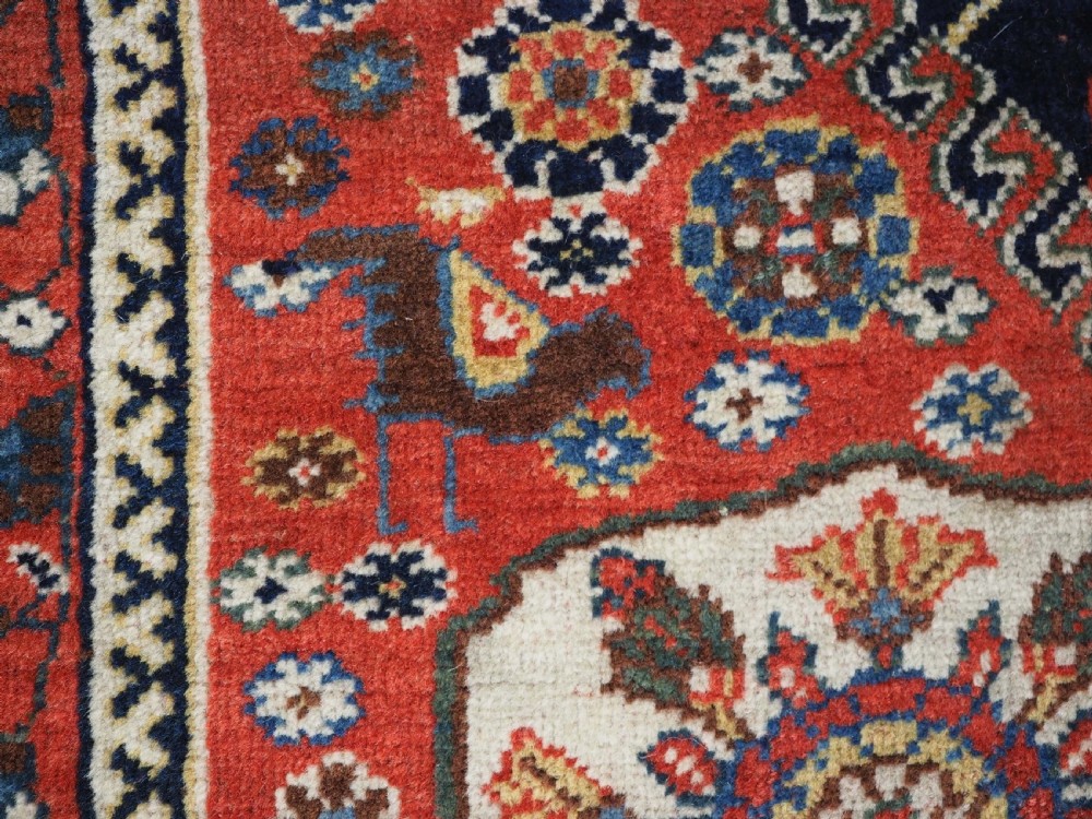 A hand-knotted wool rug featuring three diamond medallions on a dark navy field surrounded by geometric floral borders in red, ivory, and blue. View XII