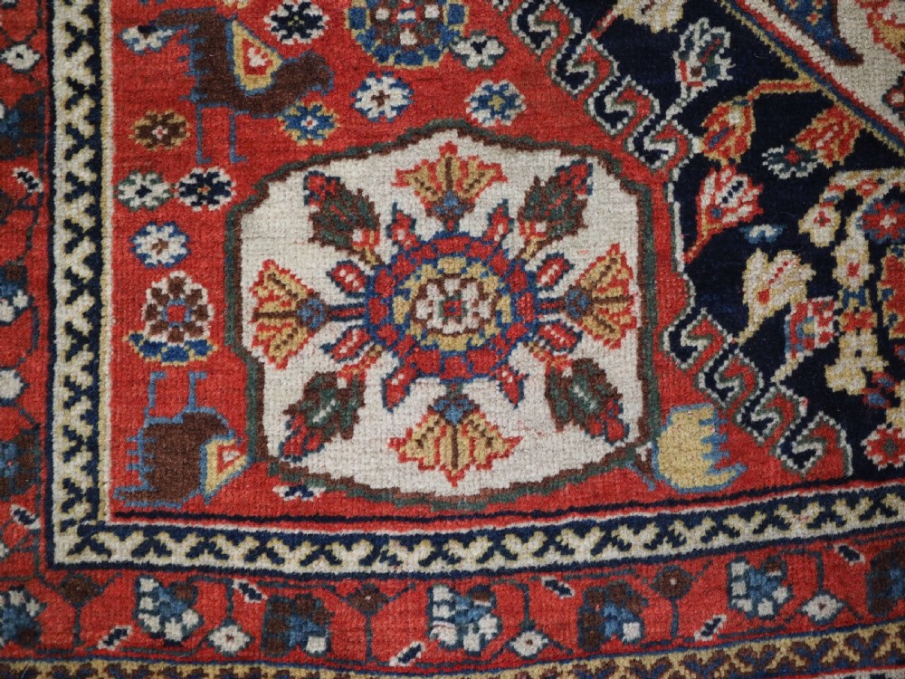 A hand-knotted wool rug featuring three diamond medallions on a dark navy field surrounded by geometric floral borders in red, ivory, and blue. View XIV